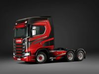 Roter Lkw ohne Anhänger vor grauem Hintergrund. Das Fahrzeug hat sechs Räder und dynamische, schwarze Grafiken an den Seiten. Die Kabine ist groß und aerodynamisch gestaltet.